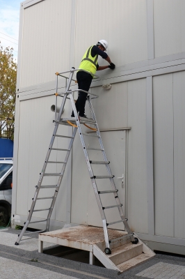 stege stående mot husvägg med person i verselkläder som jobbar